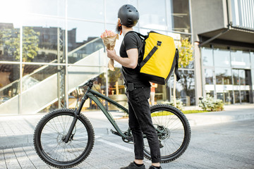Young and cheerful courier waiting with flowers for a client near the building outdoors, delivering...