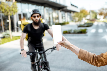 Holding a smartphone with blank screen with male courier on a bicycle on the background. Concept of a delivery mobile application