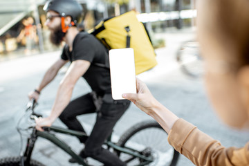 Woman client holding a smartphone with blank screen ordering some products to deliver outdoors. Concept of a delivery mobile application