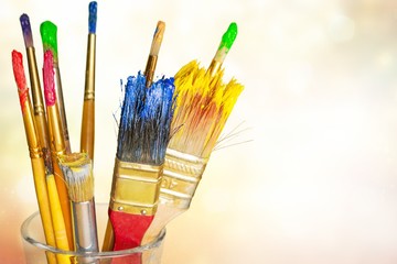 Wooden art palette with blobs of paint and a brushes on white background