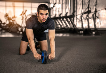 Handsome sportsman is doing ab wheel rollout exercise and looking forward while working out at...