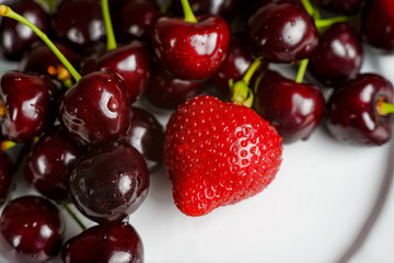 Glossy cherries on a white plate with red strawberries. Ripe and juicy cherry fruits and strawberries