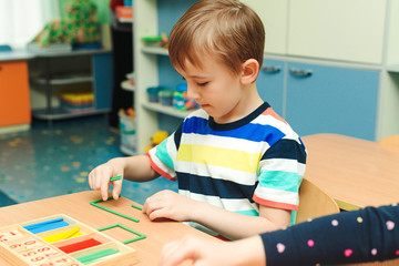 Little boy is learning math. Preschool education and development. Child makes geometric forms from colorful sticks.