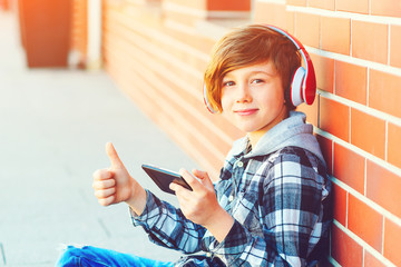 Schoolboy wearing headphones and using mobile phone on a break. Happy smiling boy plays games...