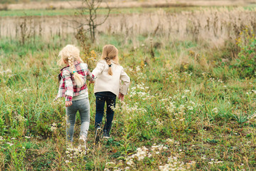 Friendship, childhood, leisure and family concept. Two little girls running around holding hands in autumn park. Happy childhood. Sisters having fun together