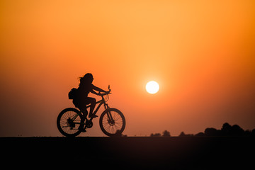 Obraz na płótnie Canvas Silhouette woman cycling on sunset background