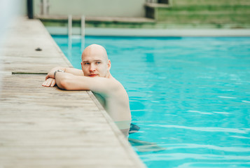Serious bald man relaxing resting in swimming pool and looking aside. Closeup portrait