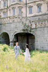 Beautiful Chinese wedding couple are walking near old building, old castle outside, vintage palace outdoor. Amazing wedding couple. Pretty bride and stylish groom.