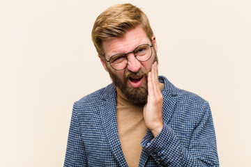 young blonde businessman holding cheek and suffering painful toothache, feeling ill, miserable and...