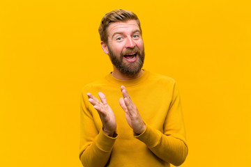 young blonde man feeling happy and successful, smiling and clapping hands, saying congratulations...