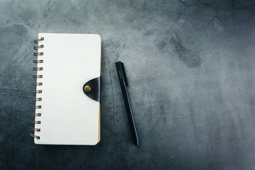 Notebook and pen on black cement background, top view.