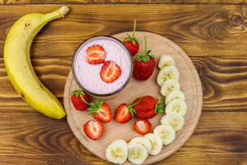 Glass of fresh smoothie of strawberry and banana on a wooden table. Top view