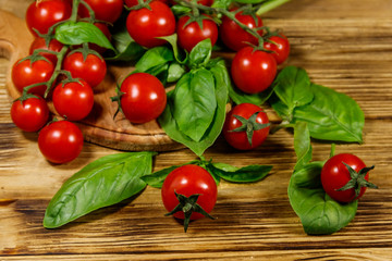 Fresh cherry tomatoes with green basil leaves on a wooden table