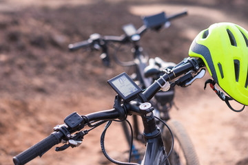 Handlebar of a black electric bicycle and view of the electronic device  recording time  and distance control. Suitable for elderly people. Yellow helmet. Outdoor footpath