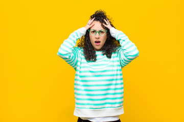 young pretty woman feeling horrified and shocked, raising hands to head and panicking at a mistake...