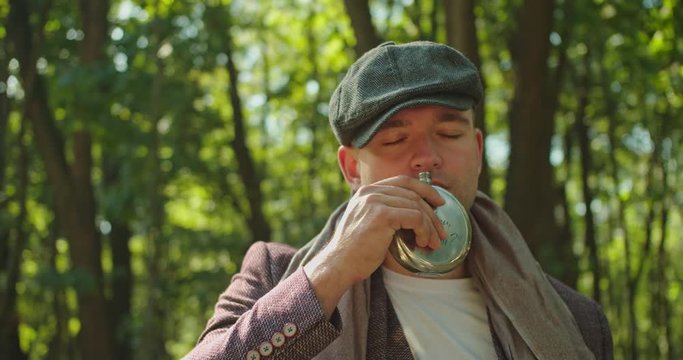 Handsome man staying on rails and drinking whiskey from flask . Alcohol cincept . 