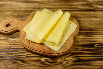 Slices of cheese on cutting board on wooden table