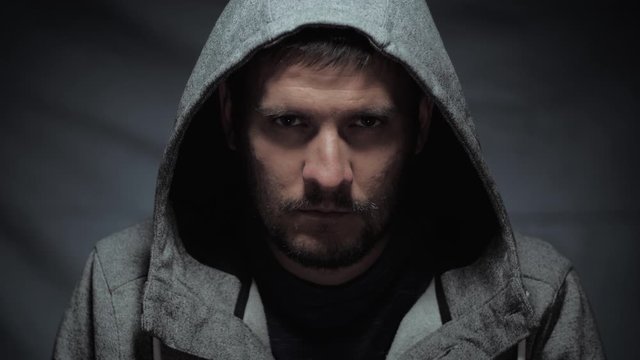 scary man portrait, portrait of an evil male in a hood looking at the camera with a cruel look on a dark background, concept of violence