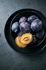 Fresh plums in dark bowl. Still life. Black background
