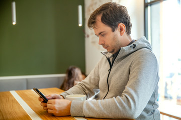 Serious man sitting in cafe with cup of coffee, working with smartphone. People using mobile phone. Businessman holding phone.