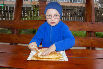 boy eating on wooden table,boy sits in glasses and eats chebureks with meat
