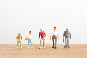 Miniature people in different ages stand on wood floor with white background