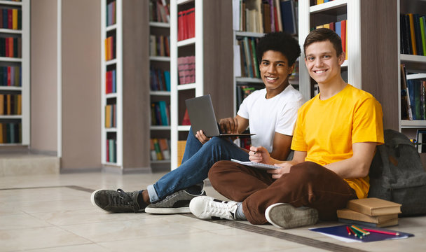 Two guys studying on floor in library, smiling at camera