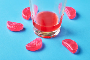Unfinished glass of juice and candies on a blue background
