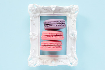 Macaroons, frame. Pink and violet macaroons on a white frame on the blue background. Sweet concept.