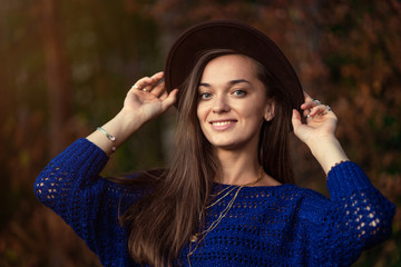 Portrait of fashionable stylish boho chic woman in hat and knitted blue sweater in autumn forest.