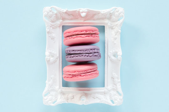 Three macaroons. Macaroons, frame. Pink and violet macaroons on a white frame on the blue background. Sweet concept.