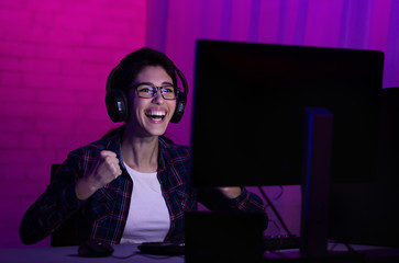 Female gamer win game, wearing headphones and rejoicing - obrazy, fototapety, plakaty