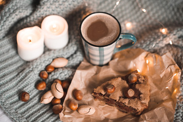 Tasty charlotte pie with nuts, cup of coffee with milk and burning candles staying on knitted cloth in bed close up. Good morning. Winter holiday season. Breakfast.