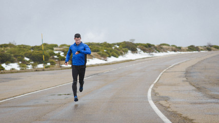 Full length athlete timing outdoor running workout on winter mountain road under the snow.