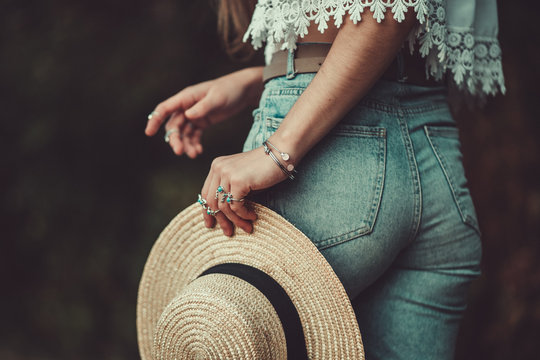 Stylish fashion woman in jeans shorts and in a white short blouse with silver turquoise rings holds a straw hat. Denim style