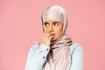 scared muslim girl in hijab biting nails, isolated on pink
