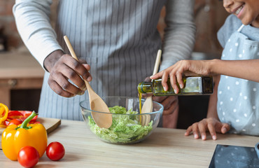 Little girl adding olive oil to healthy veggies salad