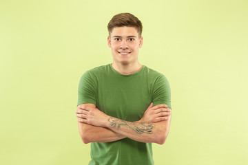 Caucasian young man's half-length portrait on green studio background. Beautiful male model in...