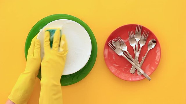 Female hands in yellow rubber gloves washing dishes in kitchen. Housework. Top view