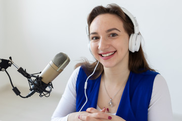 Radio host concept - Woman working as radio host sitting in front of microphone over white...