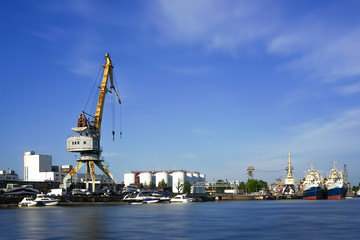 Fototapeta na wymiar The seaport at the river Pregol with ships and cargo cranes on background of blue sky.