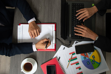 Top view businessmen working at computer and writing surrounds chart papers with red notebook,...