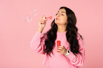 smiling brunette girl blowing soap bubbles isolated on pink