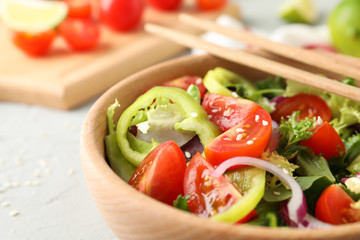 Salad with sesame and wooden board on grey background, close up