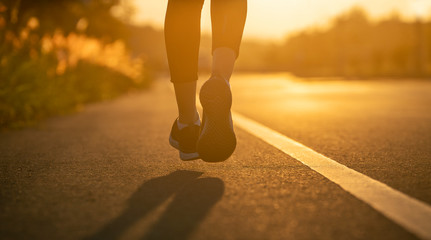Runner feet running on road closeup on shoe. Woman fitness sunrise jog workout wellness concept....