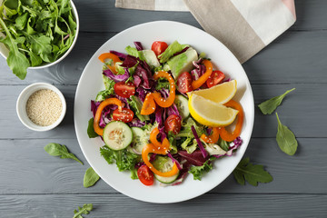 Plate with salad and ingredients on wooden background, top view