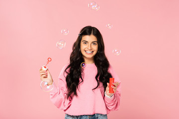 happy beautiful girl blowing soap bubbles isolated on pink