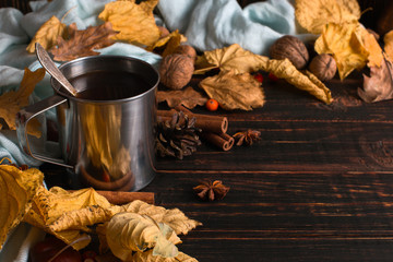 Iron mug with black coffee, spices, on a background of a scarf, dry leaves on a wooden table. Autumn mood, a warming drink. Copy space.
