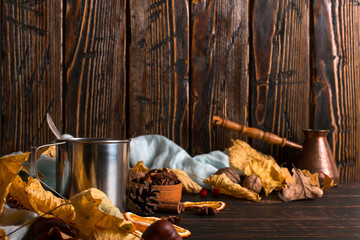 Iron mug with black coffee, spices, dry oranges, on a background of a scarf, dry leaves on a wooden table. Autumn mood, a warming drink. Copy space.