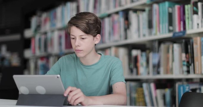 High school male student studying with digital tablet in library - Powered by Adobe